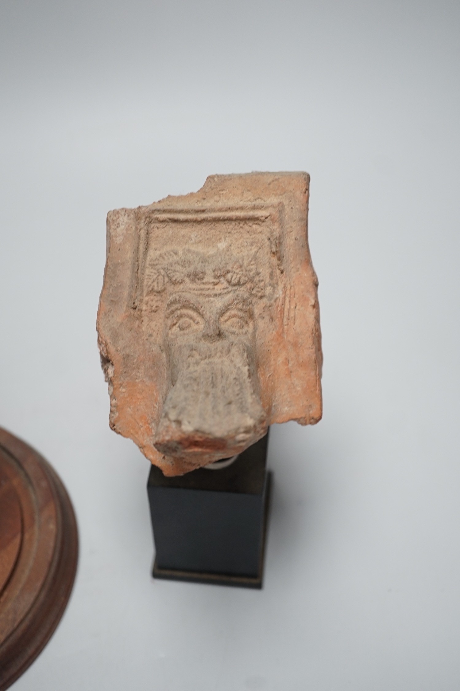 A Hellenistic terracotta brazier fragment with Dionysos mask, 2nd-1st century BCE., and a bronze fragment of a votive figure or figure of a goddess, probably Etruscan, 13.5 cm high excluding stand